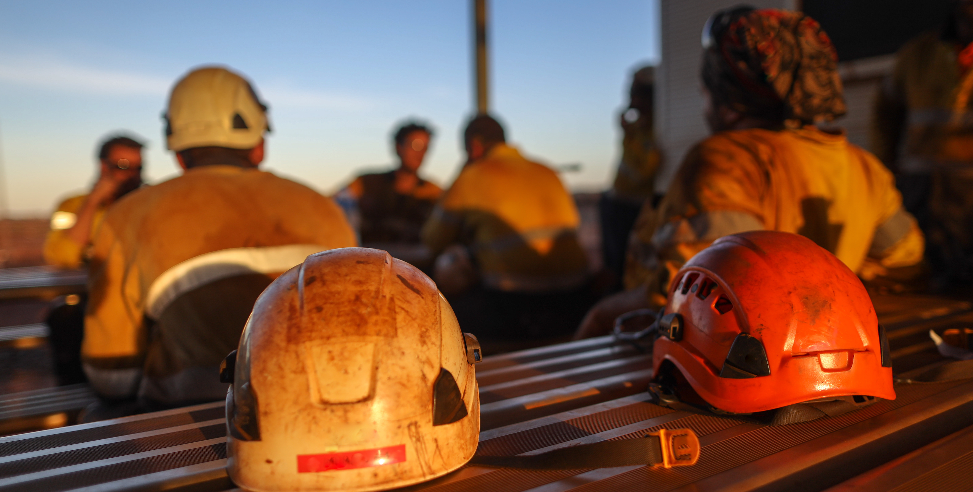 Work helmets on table with workers in the background