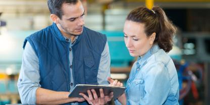 A man and women in a warehouse. They are looking at a tablet.